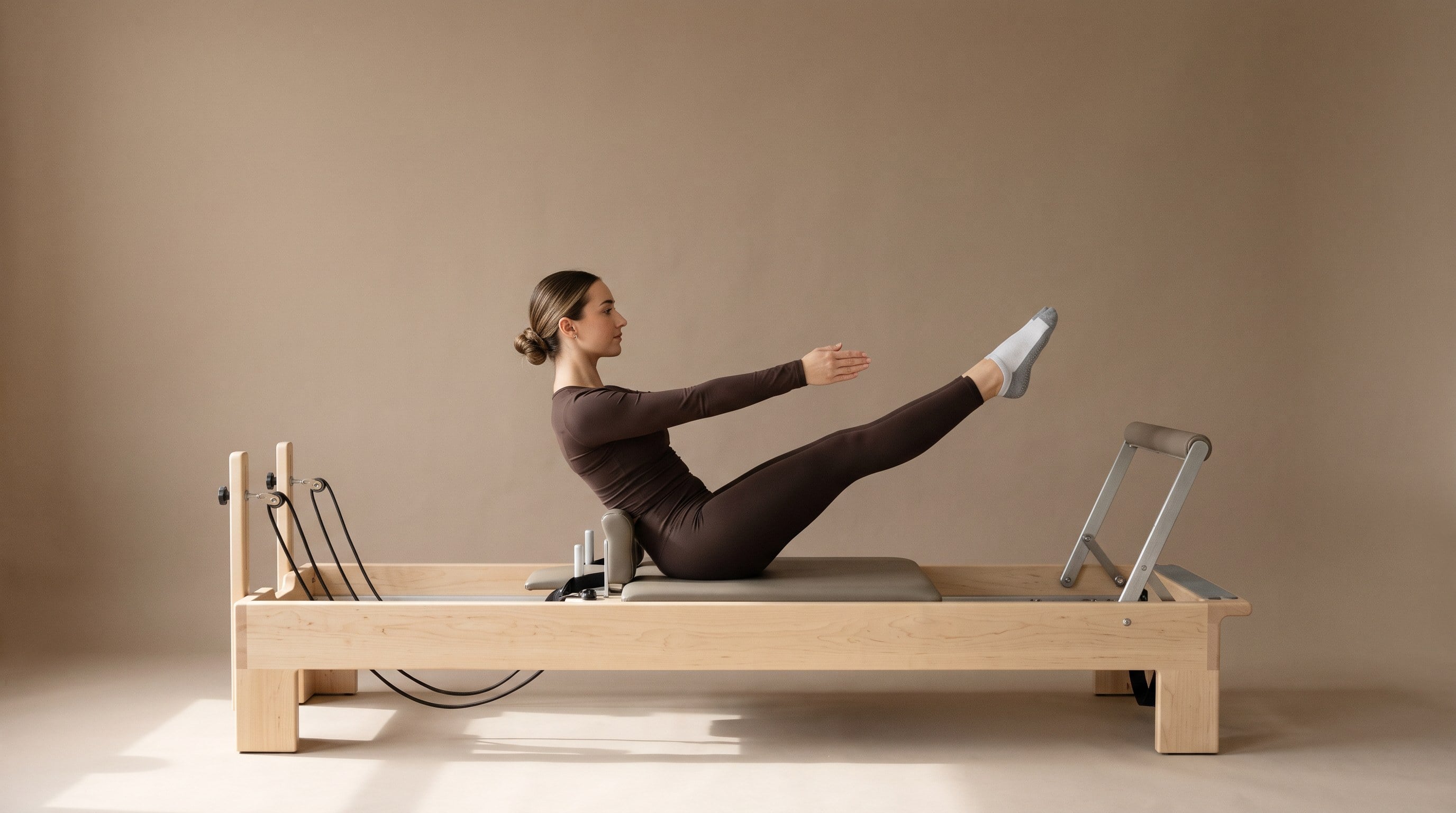 A woman in an espresso set holding a teaser on a maple reformer